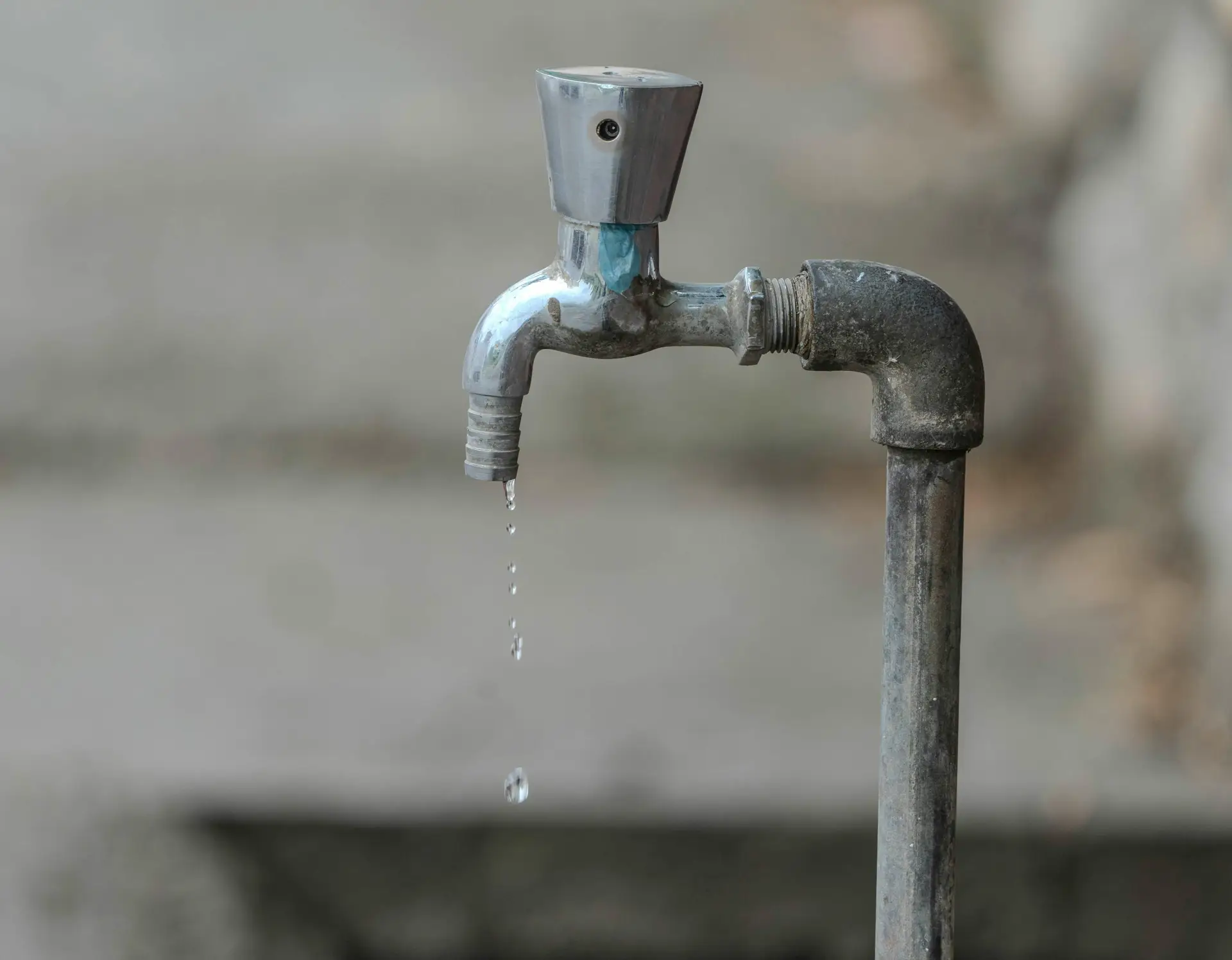 Close-up image of an outdoor water tap with a single droplet falling, highlighting water conservation.